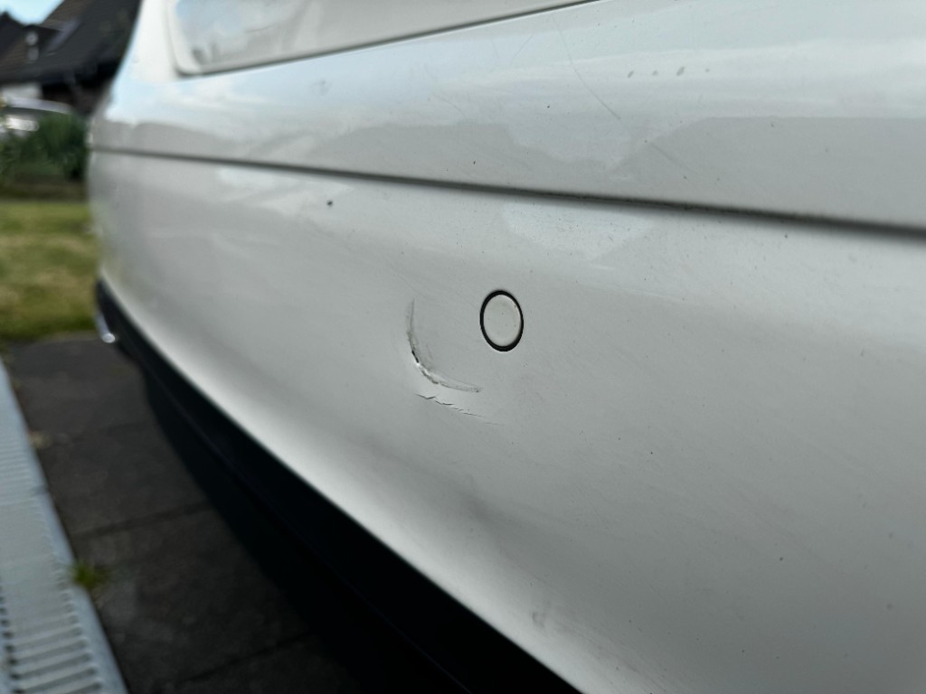 Lackkratzer am weißen Stoßfänger neben Parksensor